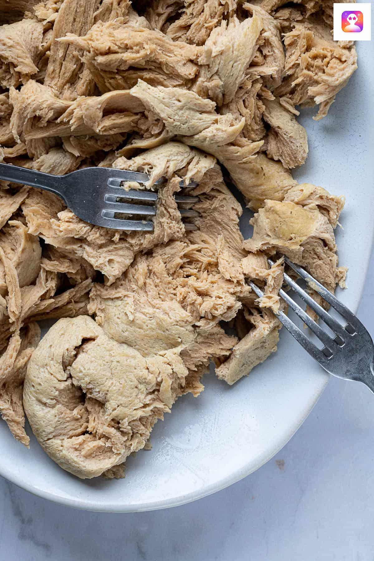 The seitan being shredded with two forks.